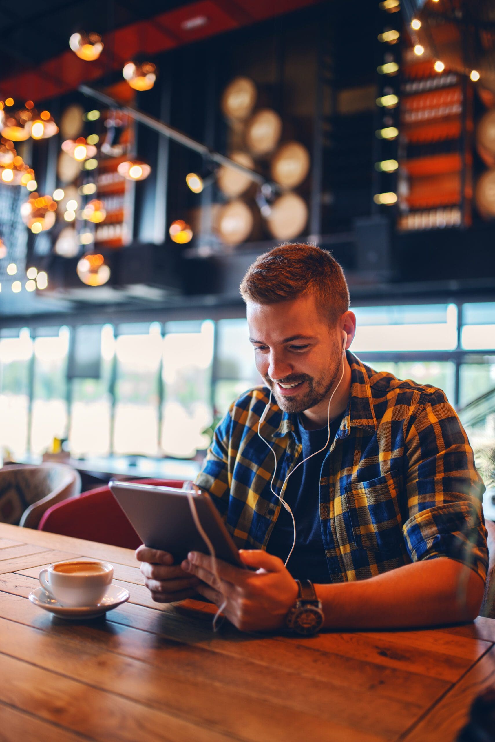 Smiling young man chilling at coffee shop, surfing on the internet, listening music.